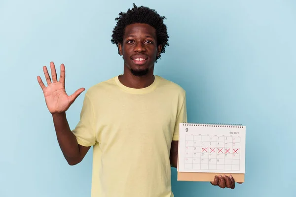 Jovem Homem Afro Americano Segurando Calendário Isolado Fundo Azul Sorrindo — Fotografia de Stock