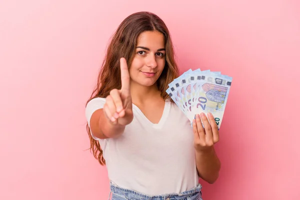 Mladá Běloška Drží Bankovky Izolované Růžovém Pozadí Ukazující Číslo Jedna — Stock fotografie