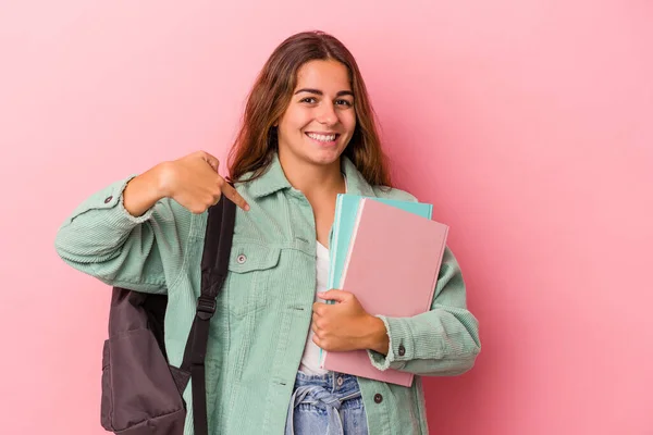 若い白人学生の女性は ピンクの背景の人に手で指差すシャツのコピースペースに本を保持します 誇りと自信 — ストック写真