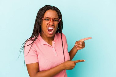 Genç Afrikalı Amerikalı bir kadın mavi arka planda izole edilmiş ve işaret parmaklarıyla fotokopi alanını işaret ederek heyecan ve arzusunu ifade ediyor..