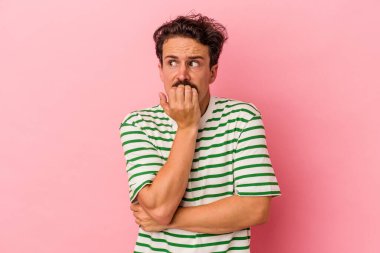 Pembe arka planda izole edilmiş, tırnak yiyen, gergin ve endişeli genç bir beyaz adam..