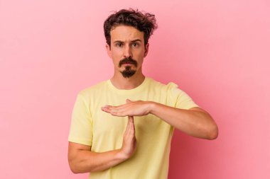 Pembe arka planda izole edilmiş genç beyaz adam bir mola hareketi gösteriyor..