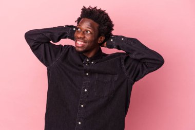Genç Afrikalı Amerikalı bir adam pembe arka planda izole edilmiş. Kendine güveniyor, elleri başının arkasında..