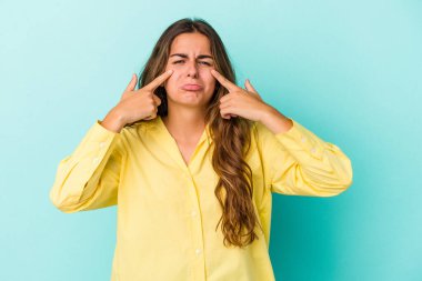 Kafkasyalı genç bir kadın mavi arka planda izole edilmiş, ağlıyor, bir şeyden memnun değil, acı ve kafa karışıklığı konsepti..