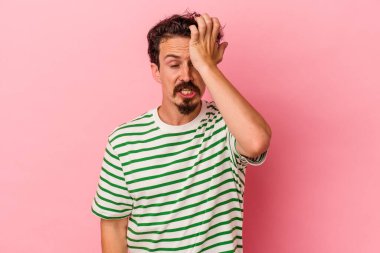 Pembe arka planda izole edilmiş genç beyaz bir adam bir şeyi unutuyor. Alnına avuç içi ve gözlerini kapatarak vuruyor..