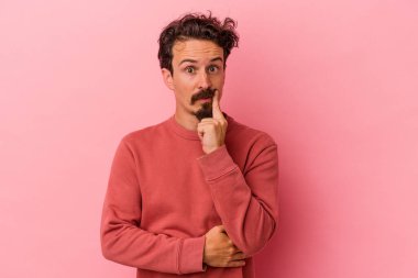 Pembe arka planda izole edilmiş genç beyaz adam şüpheli ve şüpheci bir ifadeyle yana bakıyor..