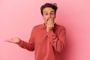 Pembe arka planda izole edilmiş genç beyaz adam, avuç içi fotokopi alanını elinde tutmaktan etkilenmiş..