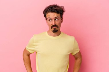 Pembe arka planda soyutlanmış, kafası karışmış, şüpheli ve kararsız genç bir beyaz adam..