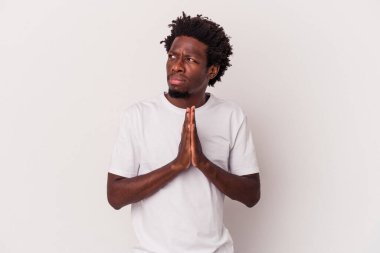 Genç Afrikalı Amerikalı adam beyaz arka planda izole edilmiş dua ediyor, bağlılık gösteriyor, dindar biri ilahi ilham arıyor..