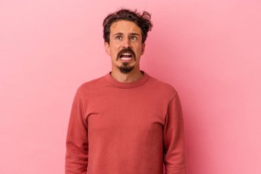Pembe arka planda izole edilmiş genç beyaz adam çok kızgın, öfkeli, hayal kırıklığına uğramış diye bağırıyor..