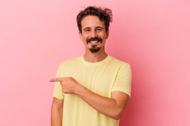 Pembe arka planda izole edilmiş genç beyaz adam gülümsüyor ve boş alanda bir şeyler gösteriyor..