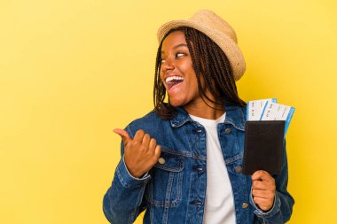Pasaportu elinde tutan Afrikalı genç bir Amerikalı kadın sarı arka planda izole edilmiş, başparmak uzakta, gülüyor ve kaygısız..