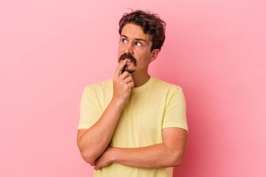 Pembe arka planda izole edilmiş genç beyaz adam şüpheli ve şüpheci bir ifadeyle yana bakıyor..