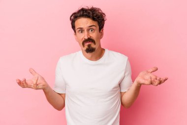 Pembe arka planda soyutlanmış genç beyaz bir adam sorgulama sırasında omuz silkiyor ve şüphe duyuyor..