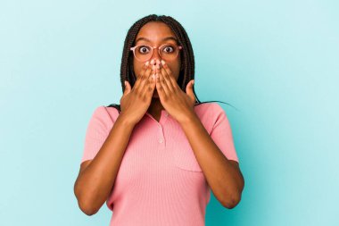 Mavi arka planda izole edilmiş genç Afrikalı Amerikalı kadın elleriyle ağzını kapatırken şok oldu..