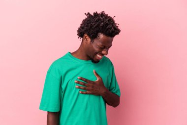 Genç Afro-Amerikan erkeği pembe arka planda izole edilmiş. Gülüyor, elini yüreğine koyuyor, mutluluk kavramını koruyor..