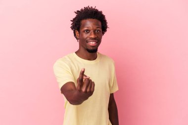 Pembe arka planda izole edilmiş genç Afro-Amerikan erkeği sanki seni davet ediyormuş gibi parmağıyla işaret ediyor..