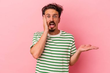 Pembe arka planda izole edilmiş genç beyaz adam, avuç içi fotokopi alanını elinde tutmaktan etkilenmiş..