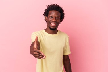 Genç Afro-Amerikalı, pembe arka planda izole edilmiş, elini kameraya uzatarak selam veriyor..