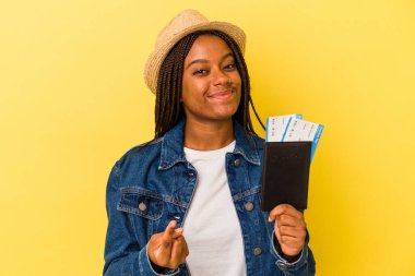 Sarı arka planda izole edilmiş pasaport taşıyan genç Afrikalı Amerikalı kadın sanki seni davet ediyormuş gibi seni işaret ediyor..