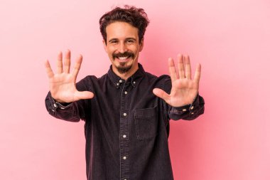 Pembe arka planda izole edilmiş genç beyaz adam on numarayı elleriyle gösteriyor..