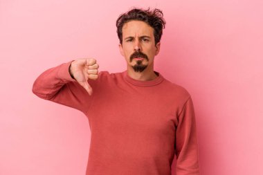 Pembe arka planda izole edilmiş genç beyaz adam baş parmağını aşağı gösteriyor, hayal kırıklığı konsepti..