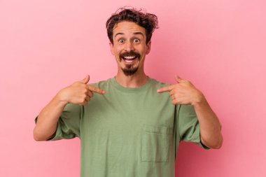 Pembe arka planda izole edilmiş genç beyaz adam parmağını göstererek şaşırdı, geniş bir gülümsemeyle..