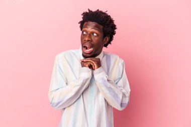 Genç Afrikalı Amerikalı bir adam pembe arka planda izole edilmiş şans için dua ediyor, hayrete düşüyor ve ağzını açıyor..