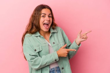 Pembe arka planda izole edilmiş genç beyaz kadın işaret parmaklarıyla işaret ederek heyecanlanıyor..