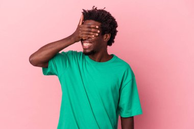 Pembe arka planda izole edilmiş genç bir Afro-Amerikan erkeği elleriyle gözlerini kapatıyor, gülümseyerek büyük bir sürpriz bekliyor..