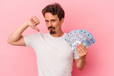Pembe arka planda izole edilmiş banknotlar tutan genç beyaz adam gururlu ve kendinden emin hissediyor, örnek olarak.