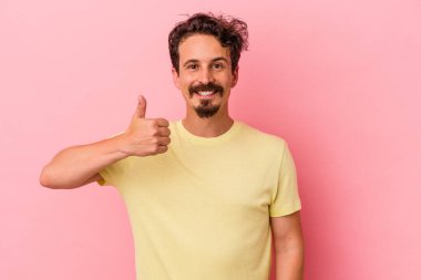 Pembe arka planda izole edilmiş genç beyaz adam gülümsüyor ve başparmağını kaldırıyor.