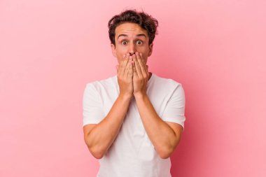 Pembe arka planda izole edilmiş genç beyaz adam elleriyle ağzını kapatırken şok oldu..