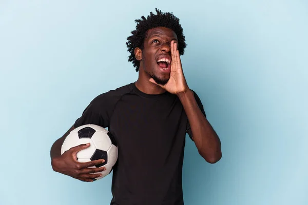Νεαρός Αφροαμερικάνος Που Παίζει Ποδόσφαιρο Απομονωμένος Μπλε Φόντο Φωνάζοντας Και — Φωτογραφία Αρχείου