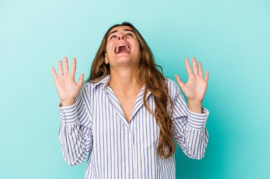 Mavi arka planda izole edilmiş genç beyaz kadın gökyüzüne haykırıyor, yukarı bakıyor, hayal kırıklığına uğramış..