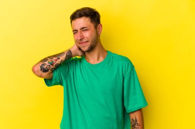 Sarı arka planda dövmeleri olan genç, beyaz bir adam stresten dolayı boynu ağrıyor, masaj yapıyor ve ona eliyle dokunuyor..