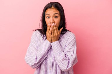 Pembe arka planda izole edilmiş, elleri endişeli görünen genç Latin bir kadın..