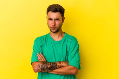 Sarı arka planda izole edilmiş beyaz dövmeli genç adam alaycı bir ifadeyle kameraya bakıyor..