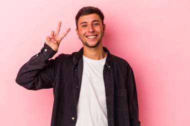 Sarı arka planda dövmeleri olan genç beyaz bir adam iki numarayı parmaklarıyla gösteriyor..