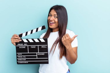 Genç Venezüellalı bir kadın mavi arka planda, parmak uzakta, gülen ve kaygısızca izole edilmiş bir klapa tutuyor..