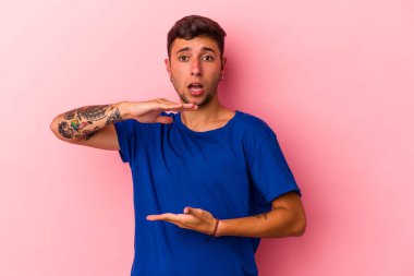 Sarı arka planda dövmeleri olan beyaz bir adam iki eliyle bir şey tutuyor, ürün sunumu..