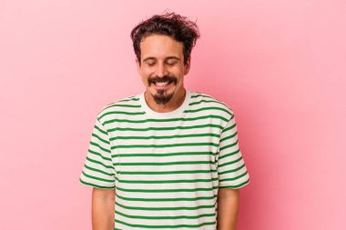 Pembe arka planda izole edilmiş genç beyaz adam gülüyor ve gözlerini kapıyor, rahatlamış ve mutlu hissediyor..