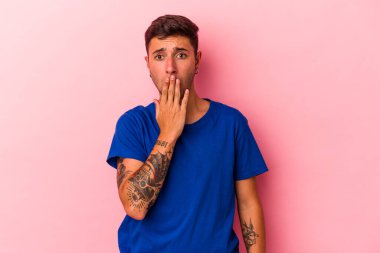 Sarı arka planda izole edilmiş, ağzı ellerle kaplanmış, yeni bir şey keşfetmek için sabırsızlanan beyaz dövmeli genç bir adam..