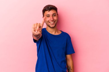 Sarı arka planda dövmeleri olan genç beyaz bir adam bir numarayı parmağıyla gösteriyor..