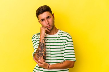 Sarı arka planda izole edilmiş dövmeleri olan genç beyaz bir adam tekrarlanan bir görevden yoruldu..