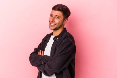 Sarı arka planda kendini güvende hisseden, kararlılıkla kollarını kavuşturan dövmeli beyaz bir genç..