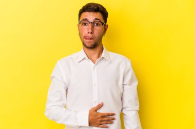 Sarı arka planda izole edilmiş beyaz dövmeli genç bir adam karnına dokunuyor, nazikçe gülümsüyor, yemek yiyor ve tatmin oluyor..