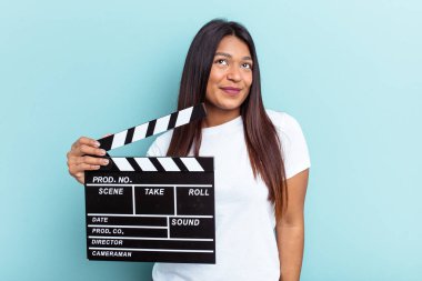 Genç Venezuelalı bir kadın mavi arka planda izole edilmiş bir alçıpan tutuyor. Hedeflerine ve amaçlarına ulaşma hayali kuruyor.