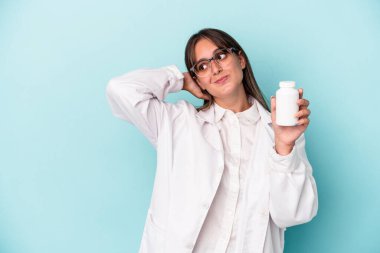 Mavi arka planda hapları tutan genç eczacı kadın kafasının arkasına dokunuyor, düşünüyor ve bir seçim yapıyor..