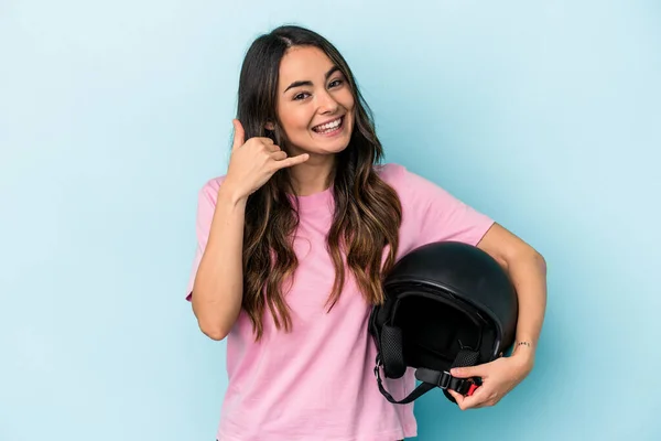 Young caucasian woman holding a motor bike helmet isolated on blue background showing a mobile phone call gesture with fingers.